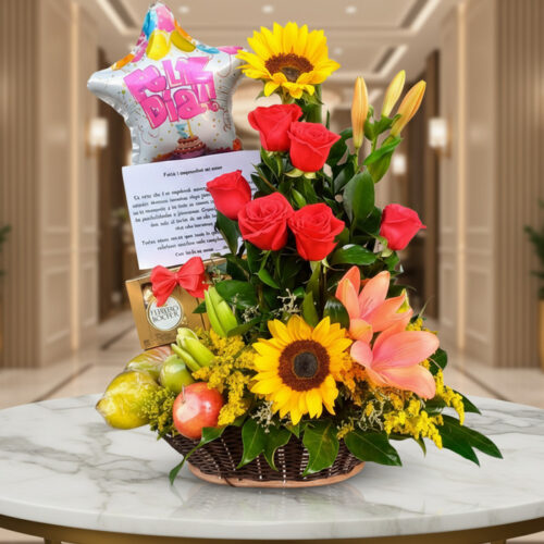 Arreglo floral premium con rosas rojas, girasoles, lirios, frutas kiwano y globo 'Feliz Día' sobre mesa de mármol en lobby el