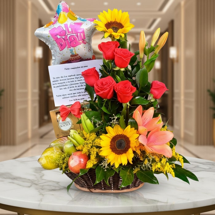 Arreglo floral premium con rosas rojas, girasoles, lirios, frutas kiwano y globo 'Feliz Día' sobre mesa de mármol en lobby el
