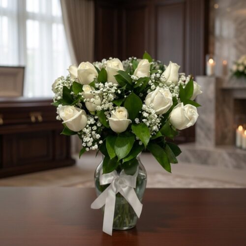 Arreglo fúnebre Pétalos del Alma con rosas blancas y follaje verde en un jarrón de cristal con lazo blanco, sobre una mesa de