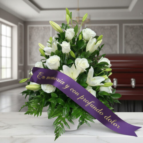 Arreglo fúnebre Piedad con rosas y lirios blancos, cinta morada con mensaje de condolencia, en sala de velación premium.