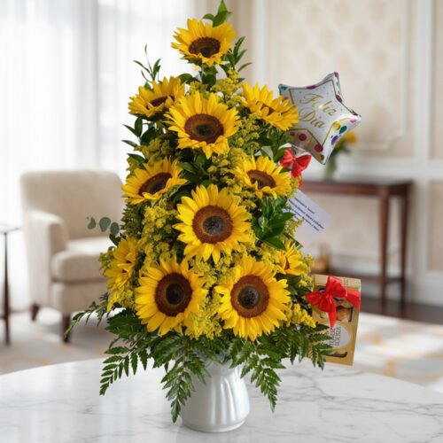 Arreglo floral premium con girasoles vibrantes y follaje verde, presentado en un jarrón blanco sobre una mesa de mármol en un